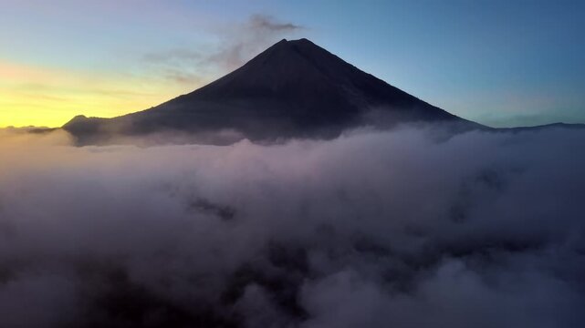 Drone panorama of Mount Semeru rising above cloud inversion at sunrise with soft pastel sky.