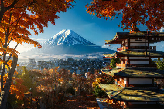 The framed by vibrant autumn leaves, Mount Fuji dominates the background, overlooking a sprawling modern city and traditional Japanese architecture.