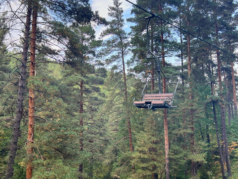 Empty chairlift seat and cable hang over tall pine trees in mountainous forest clearing