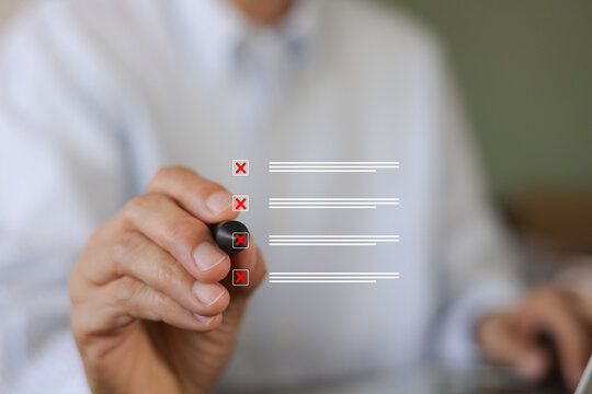 A businessman holds a marker to check red cross mark rejection symbols on a digital virtual checklist, illustrating failure, error verification, quality control, survey feedback, and wrong decisions.