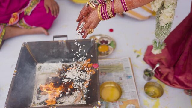 Bride in silk saree and bangles slowly drops puffed rice into a sacred fire pit during a Kannada wedding ritual.