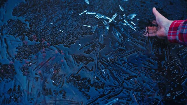 Man holding crystalline ice over water, showing detailed ice crystals and the partially frozen water surface beneath