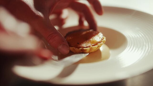 Chef delicately places a miniature tart on a plate with a knife