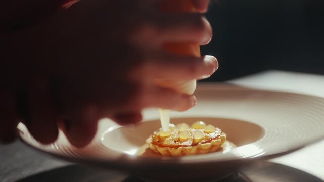 Chef adds sauce to a small tart on a white ceramic plate