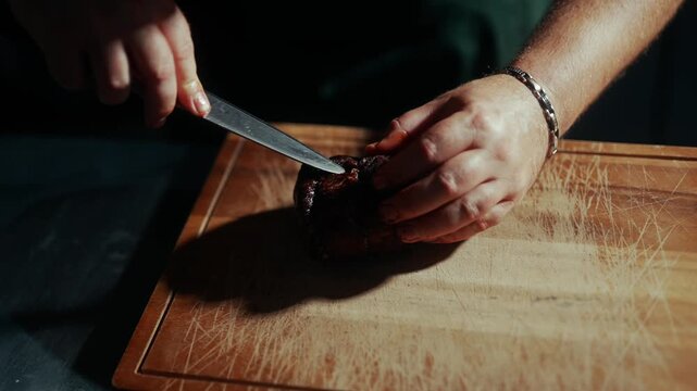 Chef cuts a dark truffle on a wooden cutting board in a kitchen
