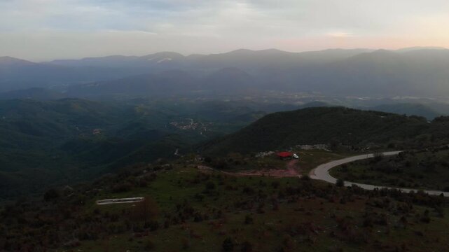 Elevated aerial perspective over Livaditis, a high-altitude mountain village in the Xanthi Region of Eastern Macedonia and Thrace, Greece. The shot captures a winding mountain road, scattered.