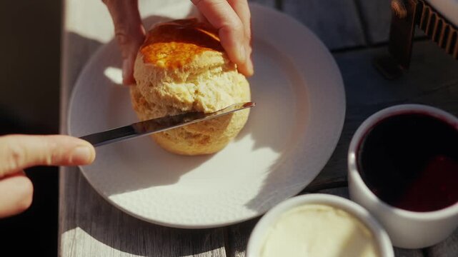 Close-up of hands spreading jam on a warm scone with butter and jam
