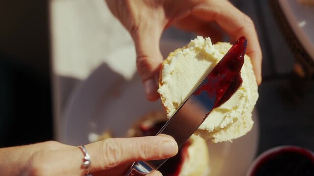 Knife spreads dark berry jam onto a fluffy biscuit in a kitchen