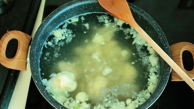 Cauliflower florets boiled in a pot with boiling water, a wooden spoon rests on the pot. Cauliflower is a light and healthy vegetable that provides about 25 calories per 100 grams and is rich in water