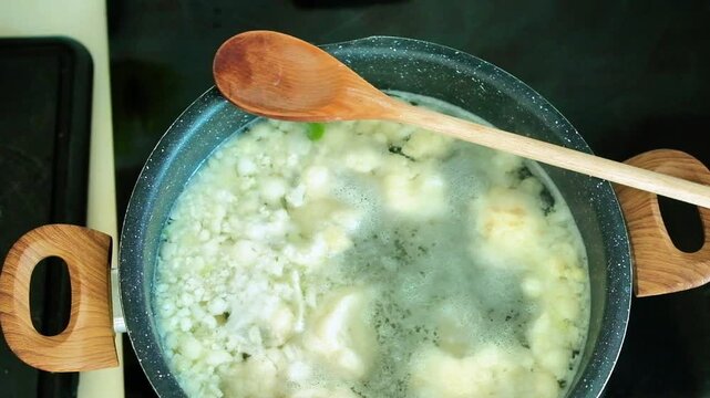 Cauliflower florets boiled in a pot with boiling water, a wooden spoon rests on the pot. Cauliflower is a light and healthy vegetable that provides about 25 calories per 100 grams and is rich in water