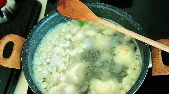 Cauliflower florets boiled in a pot with boiling water, a wooden spoon rests on the pot. Cauliflower is a light and healthy vegetable that provides about 25 calories per 100 grams and is rich in water