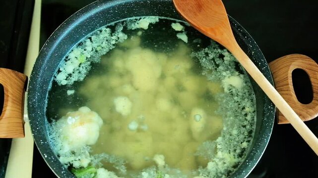Cauliflower florets boiled in a pot with boiling water, a wooden spoon rests on the pot. Cauliflower is a light and healthy vegetable that provides about 25 calories per 100 grams and is rich in water