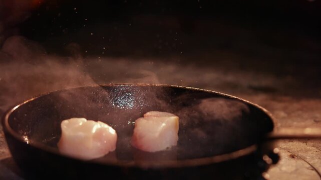 Raw scallops being added to a hot cast iron pan in a kitchen
