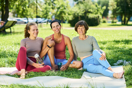 Portrait of young adult and middle aged Caucasian women sitting on exercise mats in park resting after fitness workout. Imagery suitable for wellness apps, healthy lifestyle campaigns