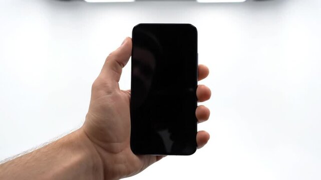 Hand holding a modern smartphone with a blank black screen against a bright white background