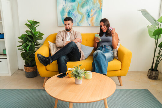 Couple sits on a bright yellow sofa, exploring a tablet while a phone rests nearby. The image conveys a warm, collaborative moment and intimate companionship with a small plant and a table nearby.
