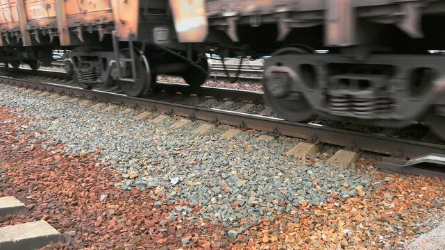 Freight train wheels pass along railway tracks above red gravel ballast