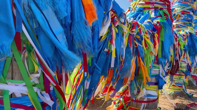 Baikal Lake. Olkhon Island. Closeup video of Serge ritual pillars with blue and colorful ribbons, Hadaks, Buddhist prayer flags with mantras near Khuzhir village. Popular landmark of Cape Burkhan