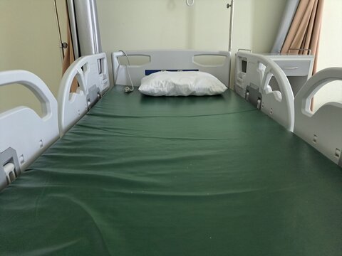 Empty hospital bed with green sheet and white pillow. Simple, clean, clinical setting with white railings. No people, no motion-quiet, still, calm atmosphere. Ideal for healthcare, recovery