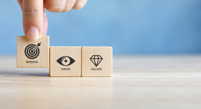 Mission, vision and values of company. Purpose business concept. Hand holds wooden cube with mission symbol and vision, values symbols on grey background. Modern flat design. Business presentation.