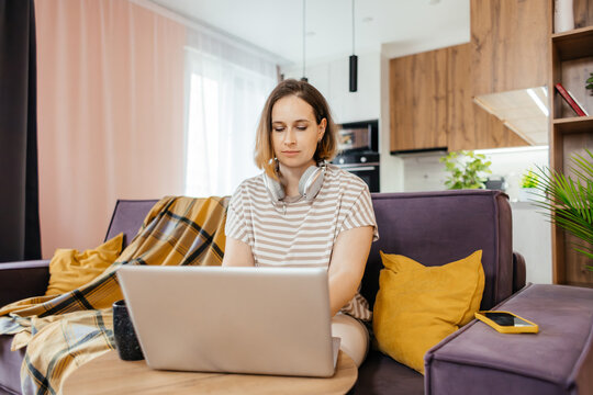 Woman with headphones use laptop on sofa at home