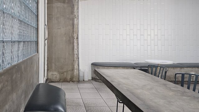 Minimalist cafe interior with concrete table, black chairs, white tiled wall, glass blocks, and industrial details, creating a clean modern urban dining space.