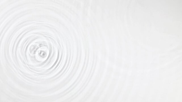 Top view of concentric water ripples on a pure white liquid surface.