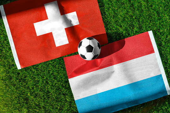 Switzerland vs. Luxembourg football match. National flags on green grass with soccer ball in the middle. Football background for international match.