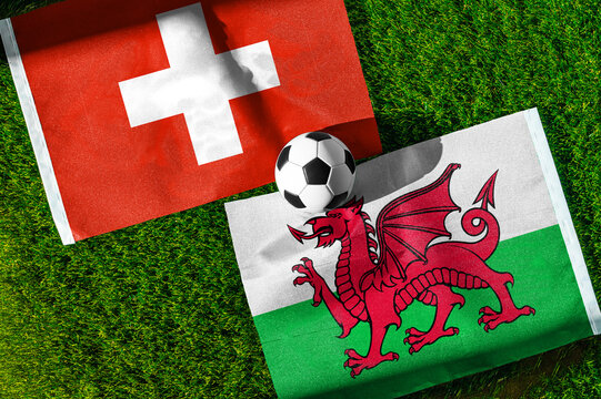 Switzerland vs. Wales football match. National flags on green grass with soccer ball in the middle. Football background for international match.