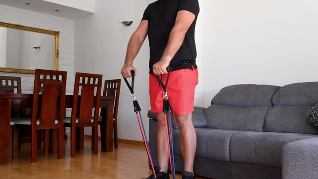 Athletic man training arms with resistance bands at home