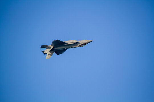 F-35A Lightning II fighter aircraft flying across a blue sky, photographed in side profile showing its distinctive stealth aircraft design.