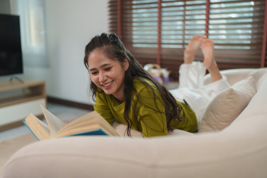 Young woman enjoying reading book on sofa at home