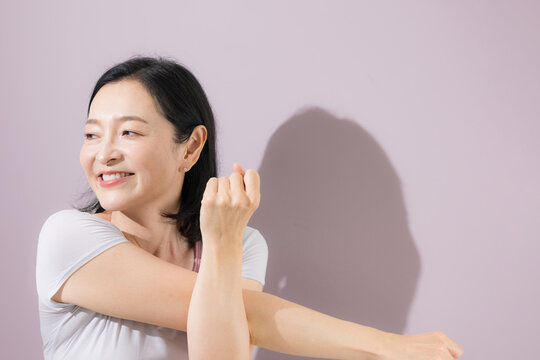 A close-up of a middle-aged Japanese woman stretching in Pilates and yoga attire with her arms outstretched, refreshing herself through the stretch