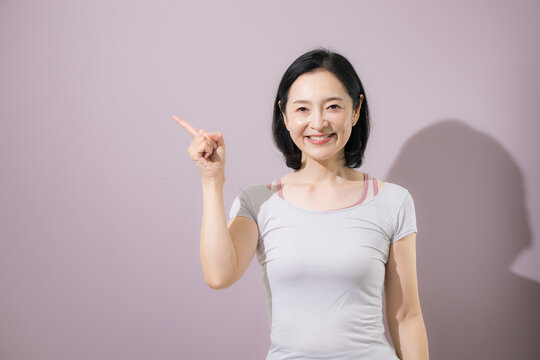笑顔で指差しやオススメをする日本人ミドル女性、商品やサービスをおすすめして案内するスポーツのフィットネスウェアの女性