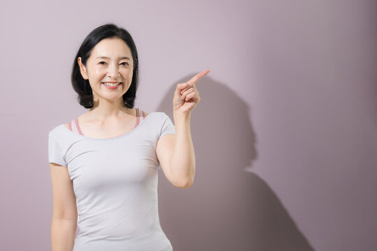 笑顔で指差しやオススメをする日本人ミドル女性、商品やサービスをおすすめして案内するスポーツのフィットネスウェアの女性