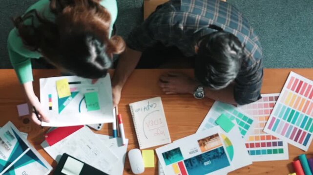 Top down view of smart designer helping manager choosing color from colored palettes. Aerial view of businessman working together and planning together while looking at logo from laptop. Symposium.