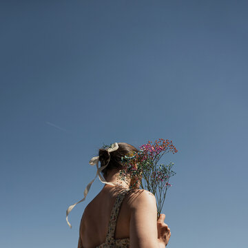 Rear View Of Woman Holding Colorful Gypsophila Bouquet Against Clear Blue Sky Background