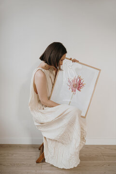 Creative Woman Holding Large Framed Botanical Poster In Neutral Interior Space