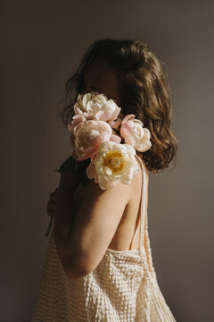 Atmospheric Moody Portrait Of Woman In Beige Dress Holding Blooming Peony Bouquet Near Face