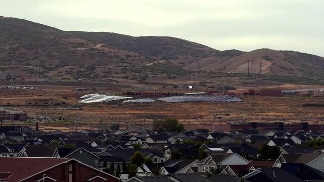 A large solar panel field array beside a suburban neighborhood, Camp Williams Army Base, and rolling hills in Bluffdale, Utah