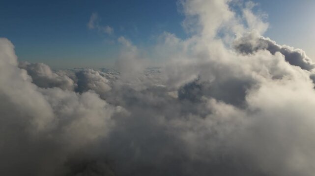 An aerial drone shot flying smoothly through fluffy white clouds under a clear blue sky during the daytime.