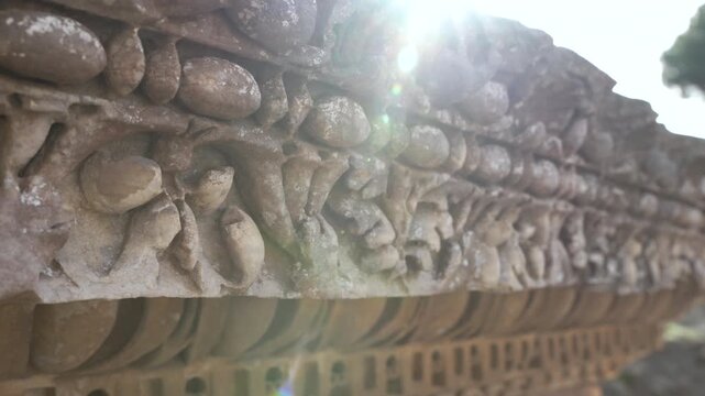 Low close-up of intricate stone cornice carving catching bright sun flare at the historic Roman site.