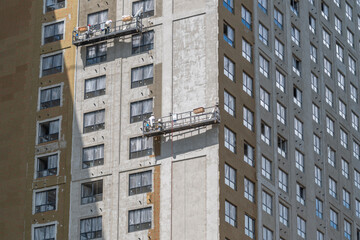 Workers fix the exterior of a tall building using a lift to apply materials to the surface © beholdereye