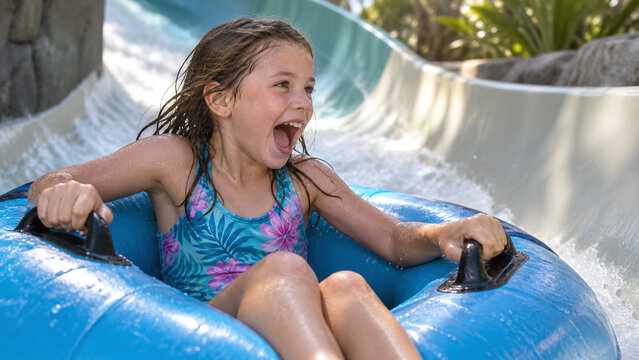 Excited young girl screaming with joy while sliding down a water slide raft