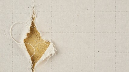 Obraz premium Close-up of torn off-white quilted fabric revealing yellow foam underlay