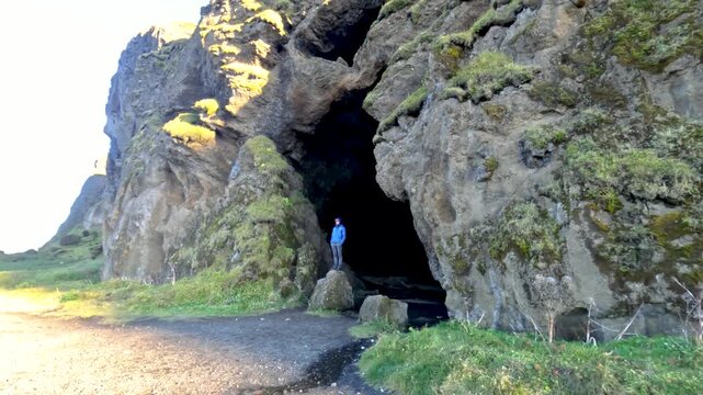Push-back shot revealing a man standing on a rock at the entrance of the massive Yoda Cave, Iceland