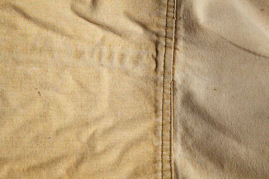 Close-up of vintage cotton canvas fabric focusing on constructive seams and stitching details. Warm beige tone, precise sewing lines and durable texture of authentic streetwear material