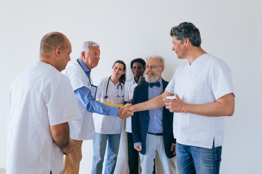 Older doctor shaking hands with man in scrubs as medical team looks on