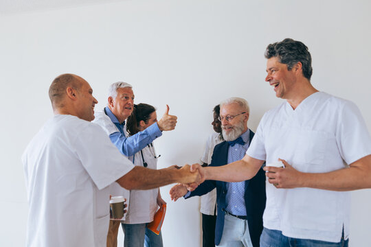 Two men in scrubs shaking hands while colleague gives thumbs up