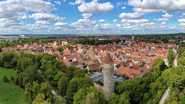 Malerische Panorama-Aussicht auf die historische Altstadt von Iphofen mit dem markanten Stadtturm, umgeben von gr&uuml;nen B&auml;umen unter einem blau-wei&szlig;en Sommerhimmel.